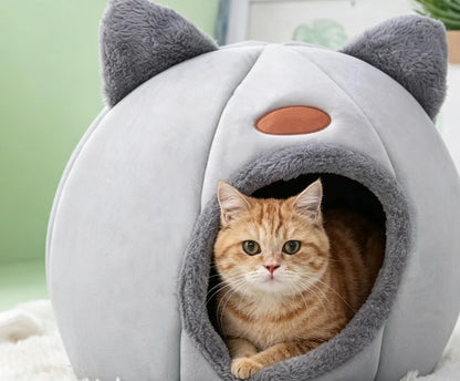 Orange cat resting inside a light gray cat ear cave bed